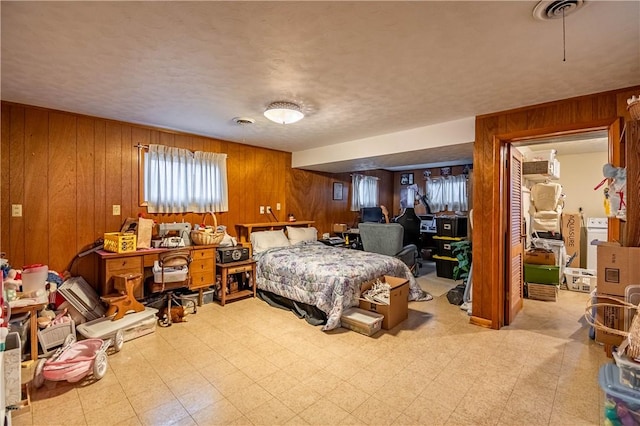 bedroom with light floors, visible vents, a textured ceiling, and wood walls