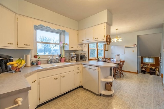 kitchen with a peninsula, white dishwasher, light countertops, pendant lighting, and a sink