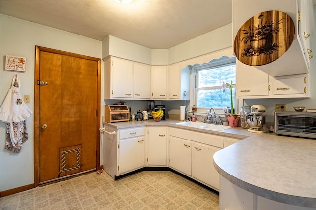 kitchen featuring a toaster, light floors, light countertops, white cabinetry, and a sink