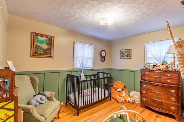 bedroom with a decorative wall, a textured ceiling, and light wood finished floors