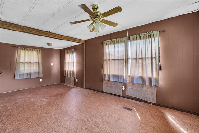 unfurnished room with a ceiling fan, visible vents, beamed ceiling, and wood walls