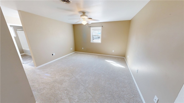 spare room with a ceiling fan, light colored carpet, visible vents, and baseboards