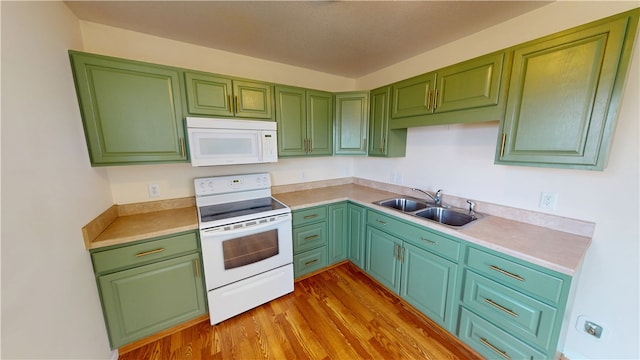 kitchen with white appliances, wood finished floors, green cabinetry, a sink, and light countertops