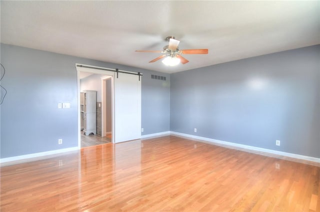 unfurnished room with a barn door, visible vents, baseboards, a ceiling fan, and light wood finished floors