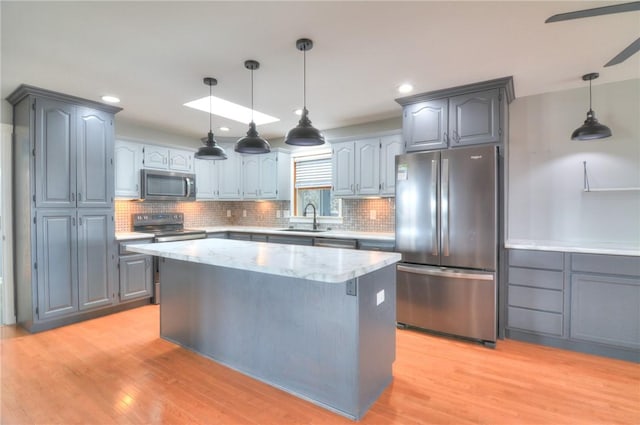 kitchen featuring appliances with stainless steel finishes, light wood-type flooring, decorative light fixtures, and a sink