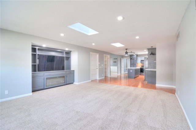 unfurnished living room featuring a skylight, recessed lighting, visible vents, light carpet, and baseboards