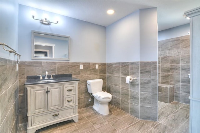 bathroom with a wainscoted wall, tile walls, toilet, vanity, and tile patterned flooring