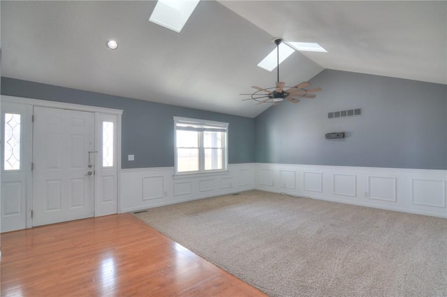 entrance foyer with vaulted ceiling with skylight, visible vents, a ceiling fan, a wainscoted wall, and wood finished floors