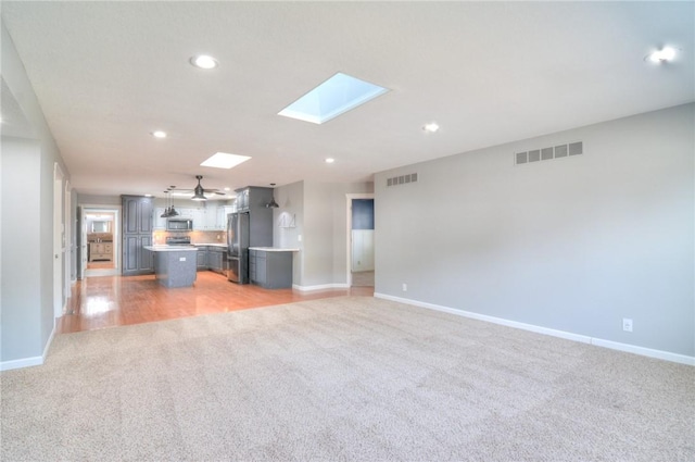 unfurnished living room featuring light carpet, a skylight, baseboards, and visible vents