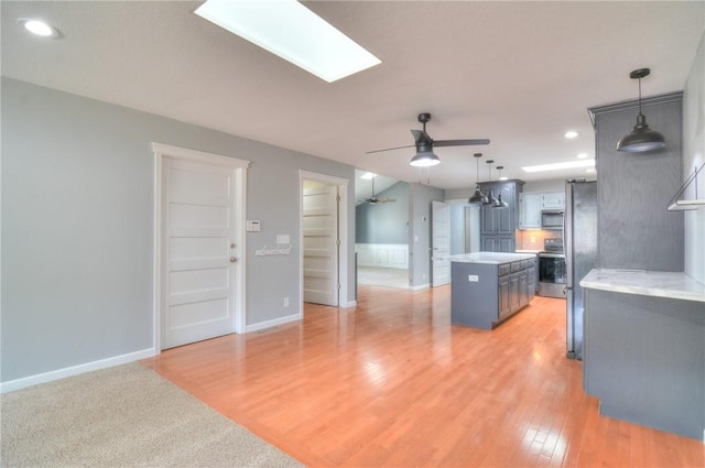 kitchen with ceiling fan, a skylight, a kitchen island, light countertops, and appliances with stainless steel finishes