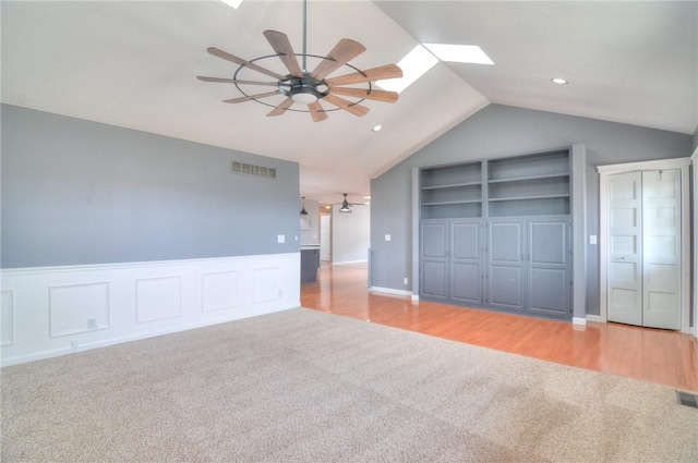 unfurnished living room with a ceiling fan, wainscoting, light colored carpet, and visible vents