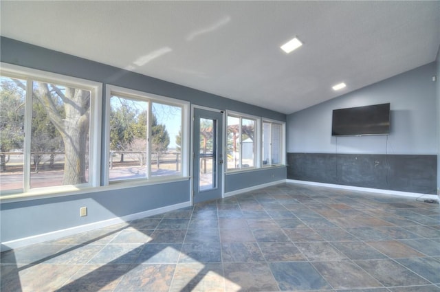 spare room featuring lofted ceiling, stone finish floor, baseboards, and a wealth of natural light