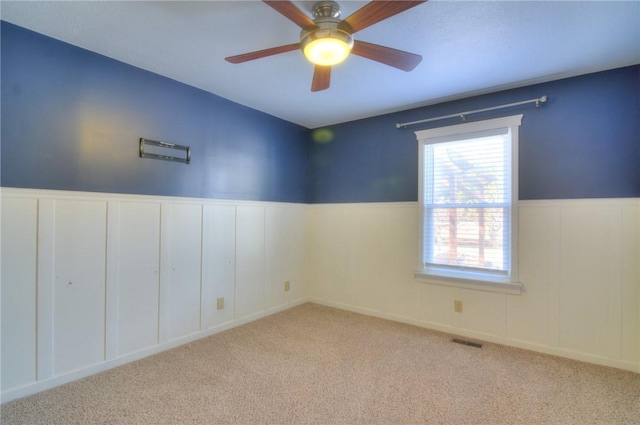 unfurnished room featuring carpet, wainscoting, visible vents, and ceiling fan