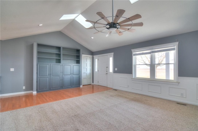 interior space with light carpet, vaulted ceiling with skylight, wainscoting, and a ceiling fan