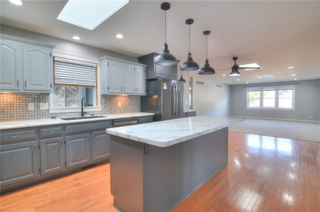 kitchen with a center island, a skylight, light wood-style flooring, freestanding refrigerator, and a sink