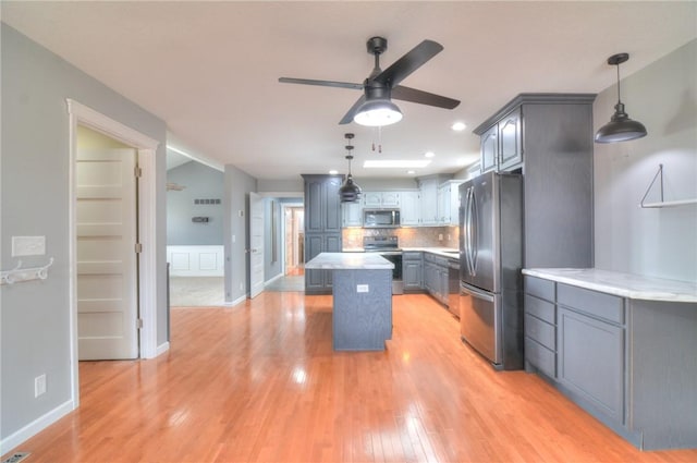 kitchen with light wood-style flooring, stainless steel appliances, light countertops, backsplash, and a center island