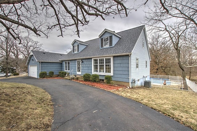 cape cod home with a garage, driveway, a shingled roof, fence, and central AC