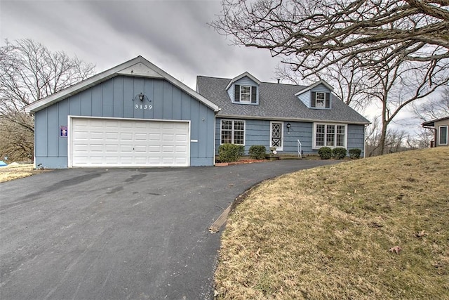 cape cod house featuring aphalt driveway, roof with shingles, an attached garage, a front lawn, and board and batten siding