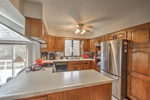 kitchen with brown cabinetry, ceiling fan, appliances with stainless steel finishes, a peninsula, and light countertops