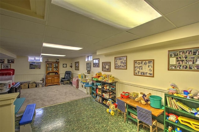 playroom with a wainscoted wall and a drop ceiling