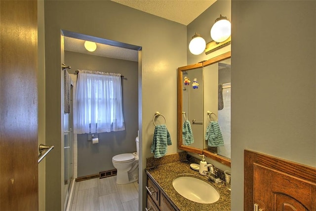 bathroom with a textured ceiling, toilet, vanity, visible vents, and a shower stall