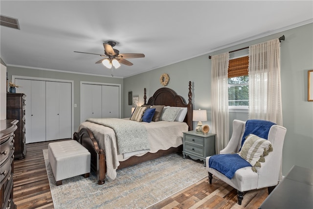 bedroom with multiple closets, dark hardwood / wood-style floors, ceiling fan, and crown molding