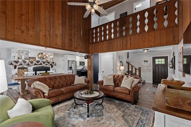 living room with hardwood / wood-style floors, ceiling fan with notable chandelier, wood walls, and a towering ceiling