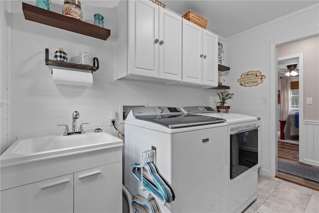 laundry area with cabinets, ornamental molding, ceiling fan, sink, and washing machine and clothes dryer