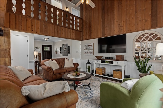 living room featuring ceiling fan, a towering ceiling, and wooden walls