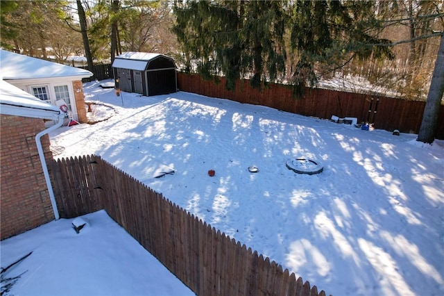 yard covered in snow featuring a storage shed, an outdoor structure, and a fenced backyard