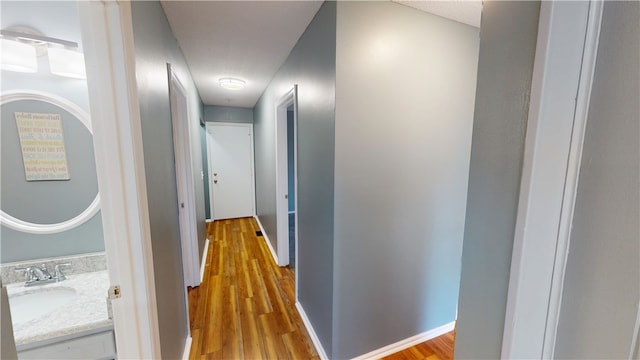 corridor with wood finished floors, a sink, and baseboards