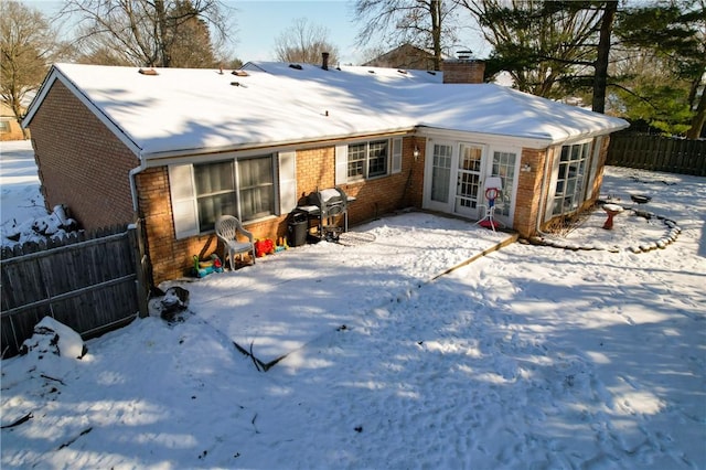 snow covered rear of property with brick siding, fence, and a chimney