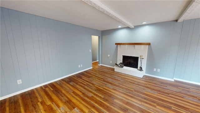 unfurnished living room featuring baseboards, wood finished floors, a textured ceiling, a fireplace, and beam ceiling