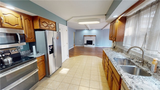 kitchen with a fireplace with raised hearth, brown cabinets, open floor plan, stainless steel appliances, and a sink