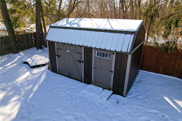 snow covered structure featuring a fenced backyard, a storage unit, and an outdoor structure