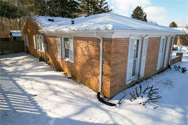 view of snowy exterior featuring fence and brick siding