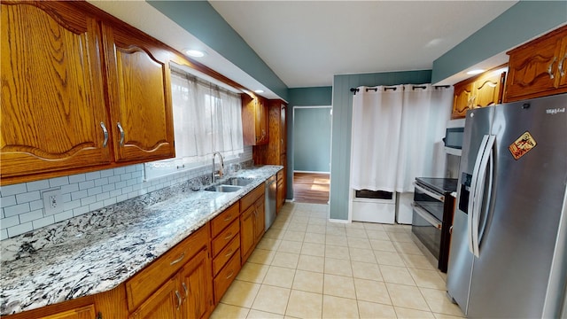 kitchen featuring brown cabinets, a sink, stainless steel appliances, backsplash, and light tile patterned flooring