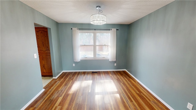 spare room featuring a notable chandelier, a textured ceiling, baseboards, and wood finished floors