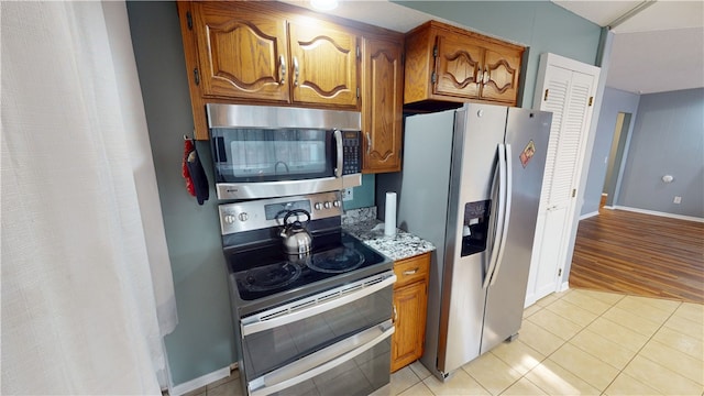 kitchen with light stone counters, light tile patterned flooring, baseboards, appliances with stainless steel finishes, and brown cabinetry