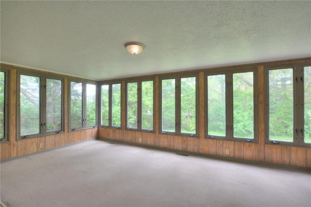 unfurnished sunroom featuring carpet floors, wood walls, a textured ceiling, and visible vents