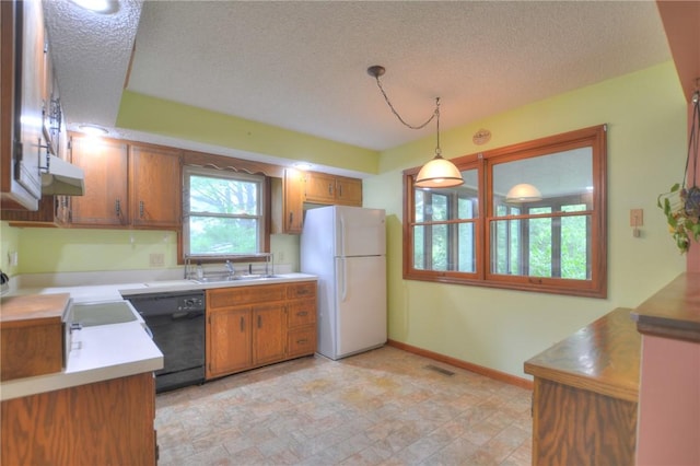 kitchen featuring brown cabinets, a textured ceiling, freestanding refrigerator, black dishwasher, and decorative light fixtures