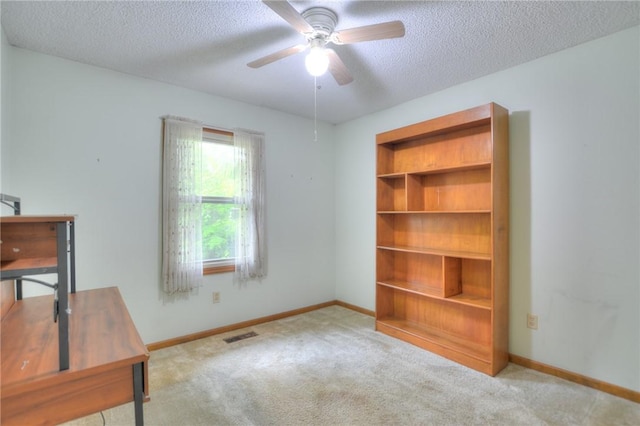unfurnished office featuring visible vents, baseboards, a textured ceiling, a ceiling fan, and carpet