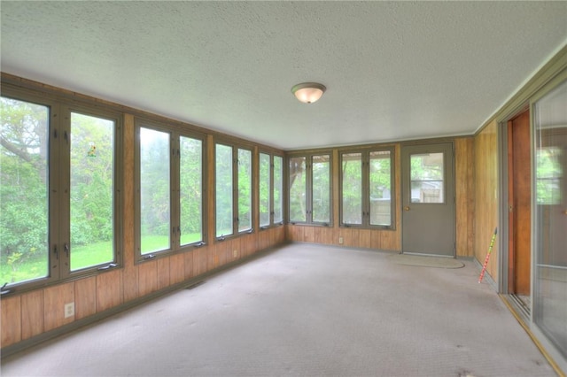 unfurnished sunroom with carpet, french doors, wood walls, and a textured ceiling