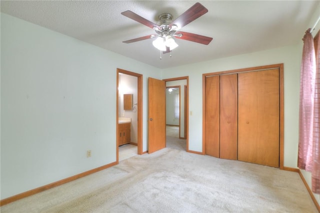unfurnished bedroom with a closet, light carpet, baseboards, ensuite bathroom, and ceiling fan