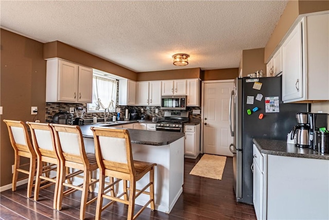 5334 Blue Mound Rd, Macon, IL 62544 - kitchen featuring appliances with stainless steel finishes, dark wood-style flooring, dark countertops, a breakfast bar, and a textured ceiling