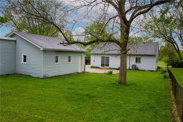 back of house with roof with shingles, fence, a lawn, and central AC