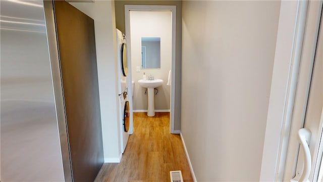 hall featuring baseboards, visible vents, stacked washer / dryer, and light wood-type flooring