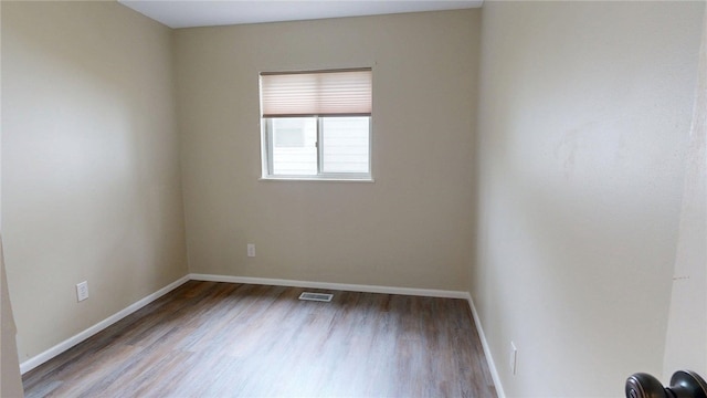 empty room featuring baseboards, wood finished floors, and visible vents