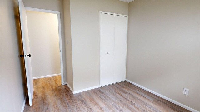 unfurnished bedroom with light wood-style floors, baseboards, and a closet