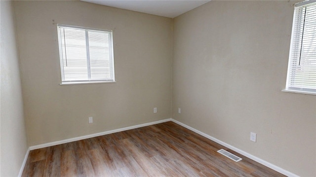 spare room with plenty of natural light, wood finished floors, and visible vents
